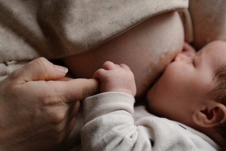 Photo d'un bébé qui tient le doigt de sa maman en faisant la tétée